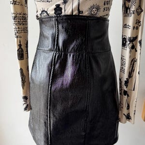 May include: A black faux leather mini skirt with a high waist and a straight cut. The skirt has a subtle sheen and is made of a smooth, textured material.
