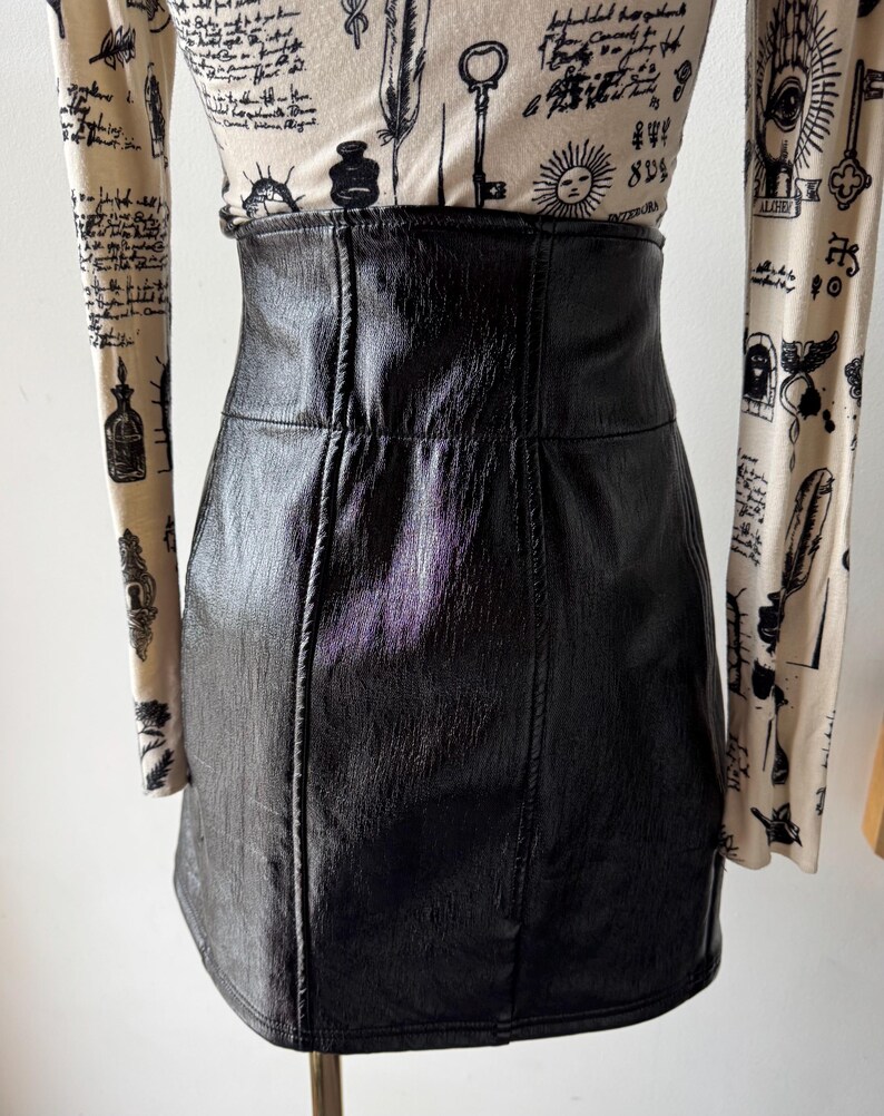 May include: A black faux leather mini skirt with a high waist and a straight cut. The skirt has a subtle sheen and is made of a smooth, textured material.