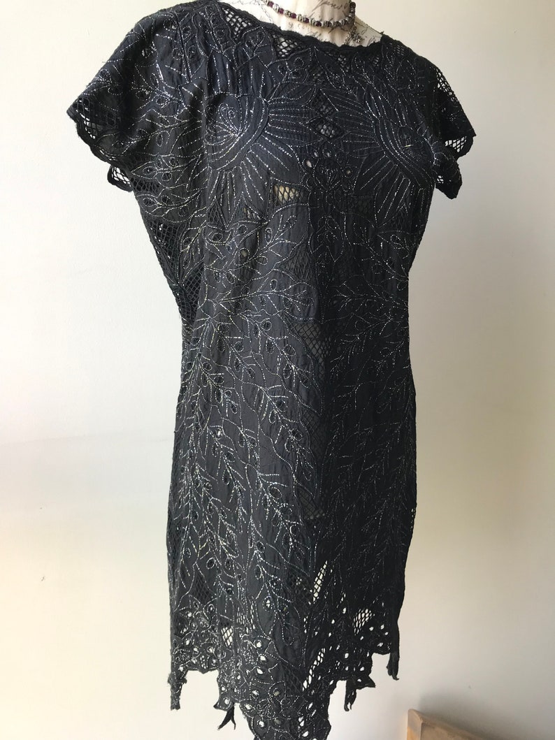 May include: A black lace dress with silver embroidery. The dress has a round neckline and short sleeves. The lace is delicate and intricate, and the embroidery is a floral design.