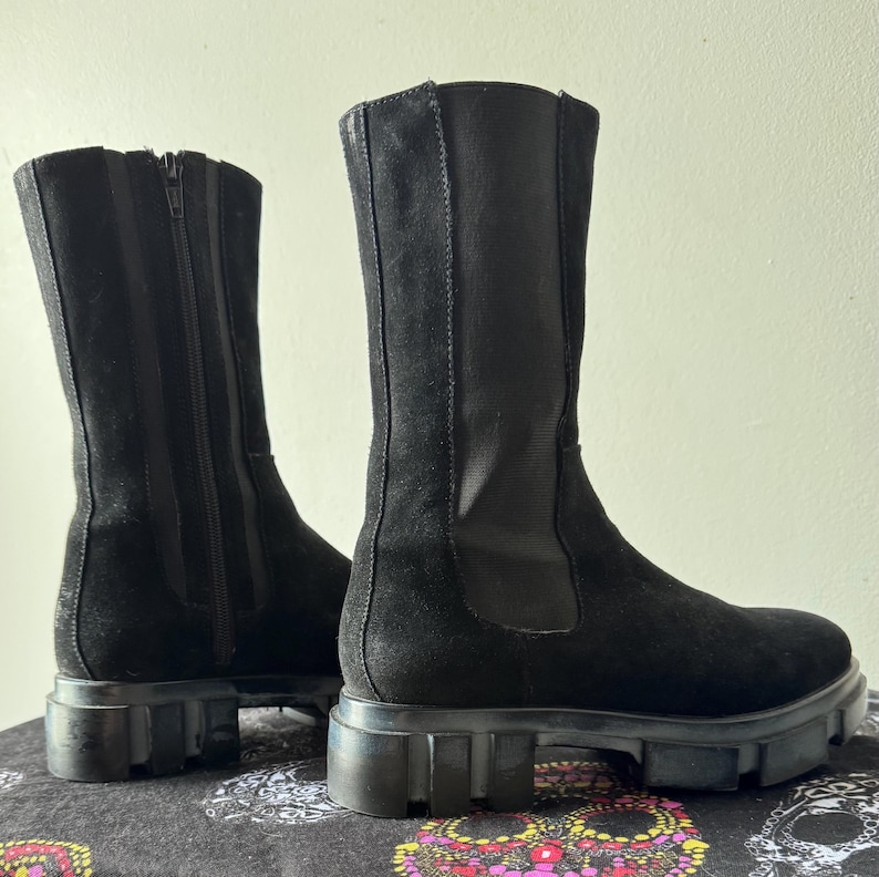 May include: A pair of black suede knee-high boots with a chunky platform sole and a zipper on the back.