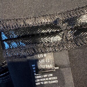 May include: Black clothing care label with instructions for washing, drying, and ironing. The label also includes size information: US 8, UK 12, 170/74A.