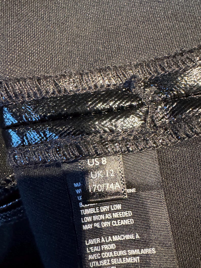May include: Black clothing care label with instructions for washing, drying, and ironing. The label also includes size information: US 8, UK 12, 170/74A.