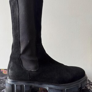 May include: Black suede ankle boots with a chunky rubber sole. The boots have a pull-on style and a slightly pointed toe.