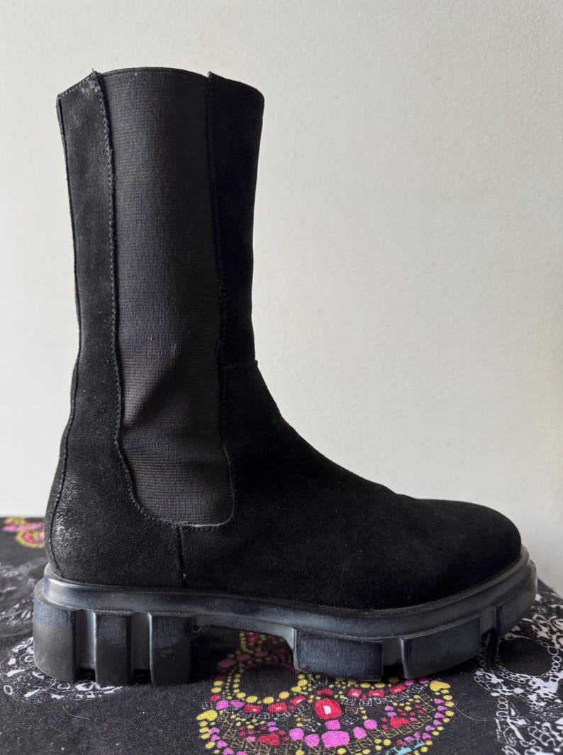May include: Black suede ankle boots with a chunky rubber sole. The boots have a pull-on style and a slightly pointed toe.