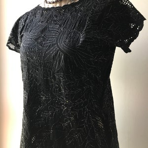 May include: Black lace top with a floral design and silver glitter accents. The top has short sleeves and a round neckline.