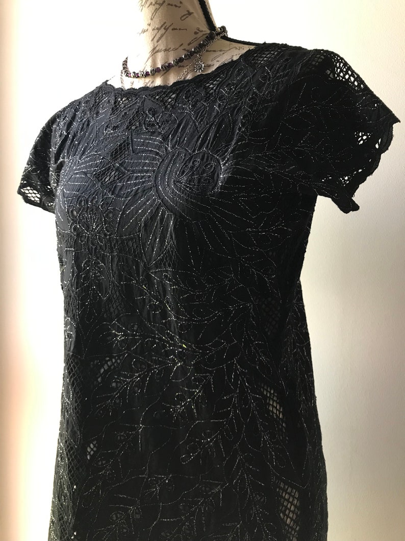 May include: Black lace top with a floral design and silver glitter accents. The top has short sleeves and a round neckline.