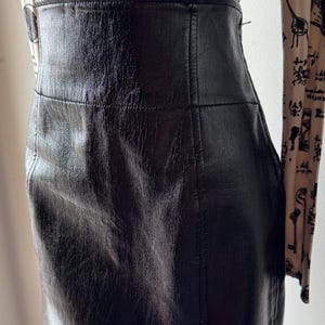May include: A black leather mini skirt with a side slit. The skirt has a smooth, shiny finish and a simple design.
