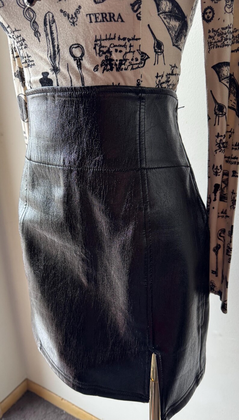 May include: A black leather mini skirt with a side slit. The skirt has a smooth, shiny finish and a simple design.