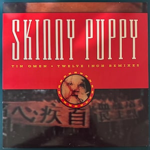Puede incluir: Una portada de disco de vinilo cuadrada con el texto SKINNY PUPPY y TIN OMEN • TWELVE INCH REMIXES en blanco y amarillo sobre un fondo rojo. Un recuadro circular muestra un primer plano de un rostro con una cruz roja sobre los ojos y la boca.