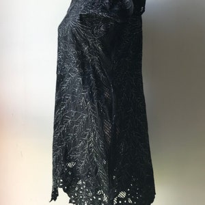 May include: A black lace dress with silver embroidery and a scalloped hemline. The dress is on a mannequin and has short sleeves.