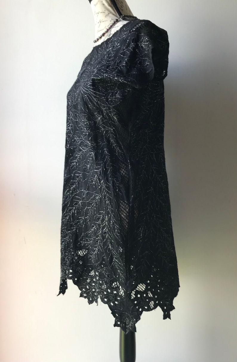 May include: A black lace dress with silver embroidery and a scalloped hemline. The dress is on a mannequin and has short sleeves.