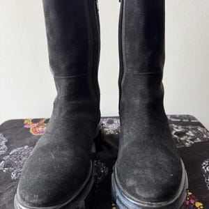 May include: A pair of black suede knee-high boots with a chunky heel and a zipper on the inside of each boot.