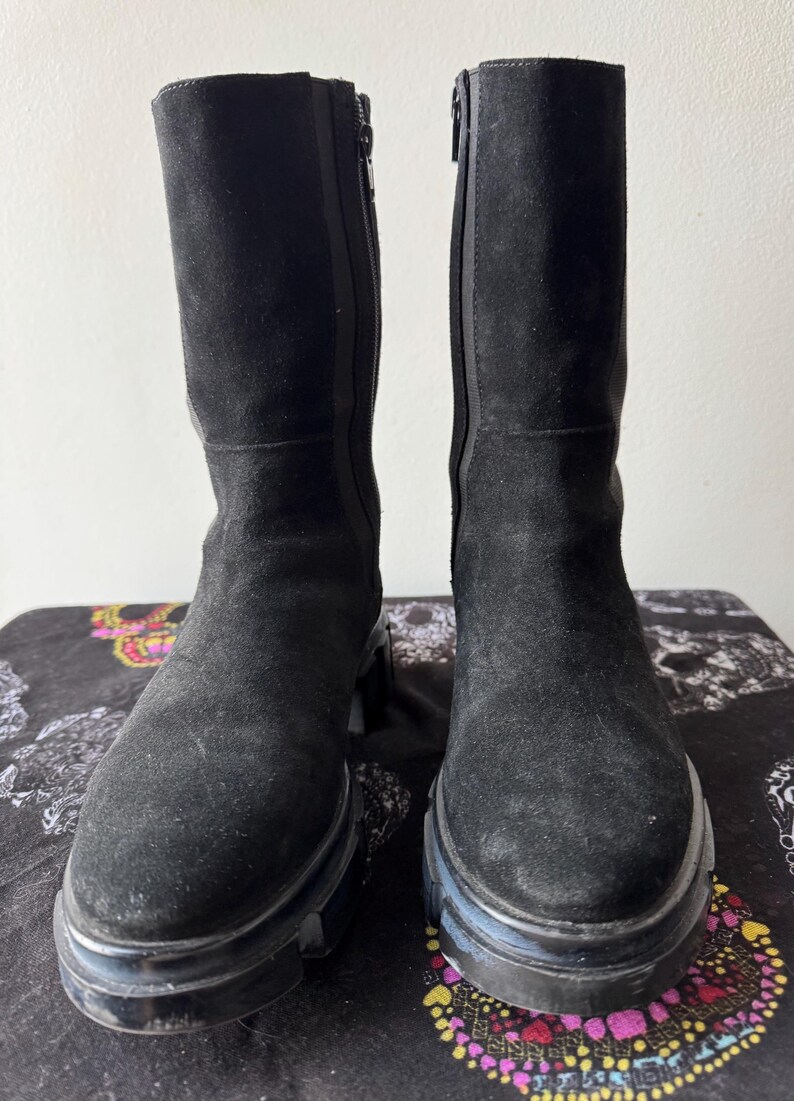 May include: A pair of black suede knee-high boots with a chunky heel and a zipper on the inside of each boot.