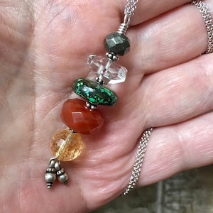 May include: A silver chain necklace with a pendant featuring a layered stack of gemstone beads. The beads are clear, green, orange, and red. The pendant is accented with small silver beads.
