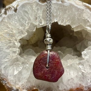 May include: A silver chain necklace with a red gemstone pendant. The pendant is wrapped in silver wire and has a silver bead accent.