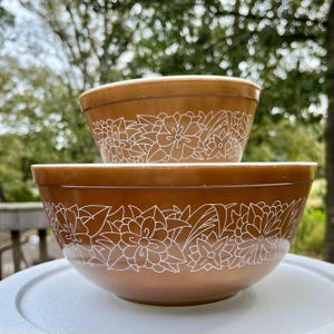 Puede incluir: Dos tazones de mezcla marrones con un diseño floral blanco. Los tazones están anidados.