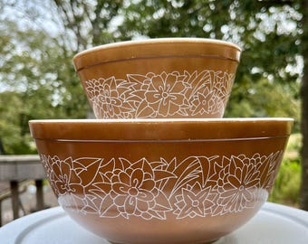 May include: Two brown mixing bowls with a white floral design. The bowls are nested together.