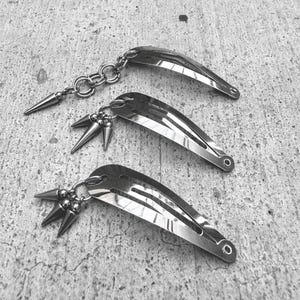 May include: A set of three ceramic mugs with a speckled, matte finish. The mugs are in shades of cream, light gray, and dark gray. Each mug has a simple, minimalist design and a rounded handle.