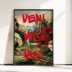 Puede incluir: Impresión artística enmarcada que presenta una pintura clásica de figuras romanas con las palabras "VENI VIDI VICI" en letras rojas audaces estilo grafiti. La obra de arte representa una escena histórica con un hombre a caballo blanco y figuras con togas.