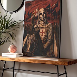 May include: Framed artwork depicting a medieval knight on horseback, raising a hand in salute. The knight wears a white tunic with a red cross, and a helmet. The background features a red sky, flags, and a line of soldiers. The artwork is displayed on a wooden bench.