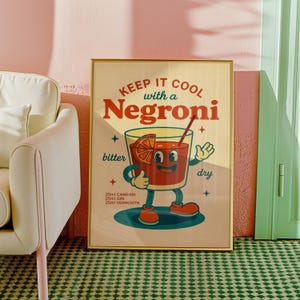 以下が含まれることがあります： 「KEEP IT COOL with a Negroni」の文字が入った、額縁に入ったヴィンテージスタイルのポスター。イラストは、笑顔の顔、オレンジスライス、ストローが付いた漫画のカクテルグラスです。ポスターには、材料としてカンパリ25ml、ジン25ml、ベルモット25mlが含まれています。