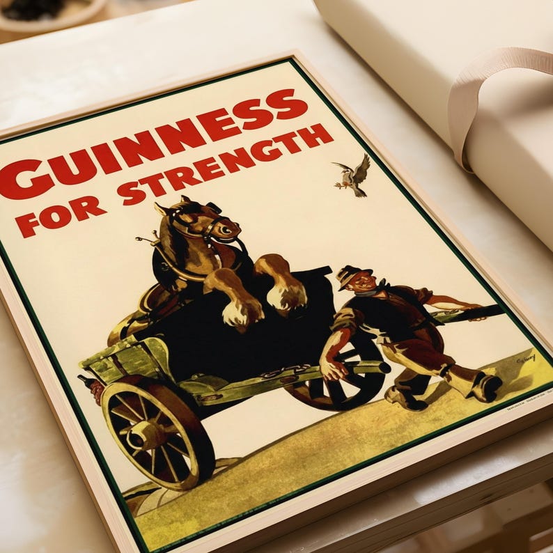 K&ouml;nnte beinhalten: Gerahmtes Vintage Guinness-Poster. Das Bild zeigt ein Pferd, das einen Wagen zieht, mit einem Mann, der ihn bergauf schiebt. Der Text "GUINNESS FOR STRENGTH" ist rot auf cremefarbenem Hintergrund. Ein Vogel fliegt in der oberen rechten Ecke.