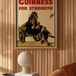 K&ouml;nnte beinhalten: Gerahmtes Vintage-Guinness-Werbeplakat mit dem roten Text "GUINNESS FOR STRENGTH". Das Bild zeigt einen Pferdewagen und einen Mann, der rennt. Eine dekorative Vase und B&uuml;cher stehen auf einem Glastisch.