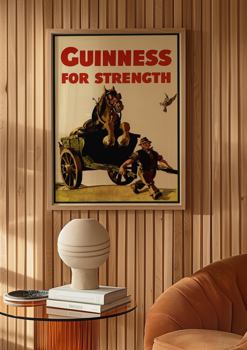 K&ouml;nnte beinhalten: Gerahmtes Vintage-Guinness-Werbeplakat mit dem roten Text "GUINNESS FOR STRENGTH". Das Bild zeigt einen Pferdewagen und einen Mann, der rennt. Eine dekorative Vase und B&uuml;cher stehen auf einem Glastisch.