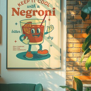 以下が含まれることがあります： ネグローニカクテルのイラストが描かれた、フレーム入りのヴィンテージスタイルのポスター。「KEEP IT COOL with a Negroni」と書かれています。カクテルは赤色でオレンジのスライスが入っており、材料が25mlの量で下に記載されています。