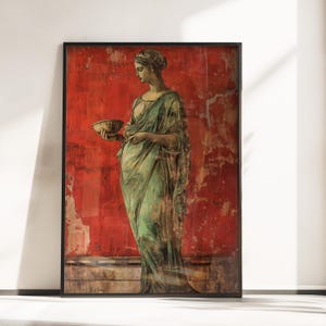 May include: Framed print of a classical figure in a flowing green robe, holding a bowl. The figure stands against a distressed red background. The artwork is framed in a black border, creating a vintage aesthetic.