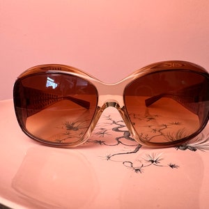 May include: Brown and beige oversized sunglasses with a tortoise shell pattern on a pink plate.