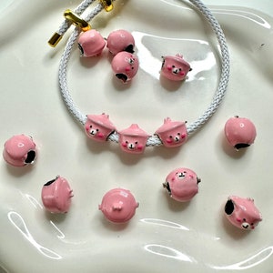 May include: A pink bracelet with a white cord and pink bear charm beads. The bracelet is on a white surface with additional pink bear charm beads.