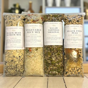 May include: Four clear plastic bags of Souper Spices products. The bags contain Black Bean Burger Mix, Vegetable Rice Mix, Salad Toppings Original, and Black Eyed Peas. Each bag has a white label with the product name and ingredients.