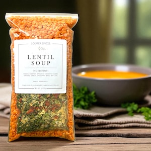 May include: A clear plastic bag filled with orange lentils and a mix of dried vegetables and herbs. The label reads "Lentil Soup" with a list of ingredients. A bowl of soup is in the background. The bag contains 8 oz (227g) of soup mix.