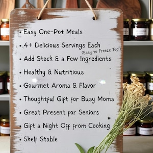 May include: A rectangular white wooden sign with distressed brown edges, hanging by a jute rope. The sign features black text listing: Easy One-Pot Meals, 4+ Delicious Servings Each (Easy to Freeze Too!), Add Stock & a Few Ingredients, Healthy & Nutritious, Gourmet Aroma & Flavor, Thoughtful Gift for Busy Moms, Great Present for Seniors, Gift a Night Off from Cooking, and Shelf Stable.