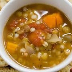 May include: A bowl of hearty lentil soup with barley, sweet potato, and tomatoes. The soup is a vibrant orange color and is garnished with fresh herbs. The soup is served with toasted bread.