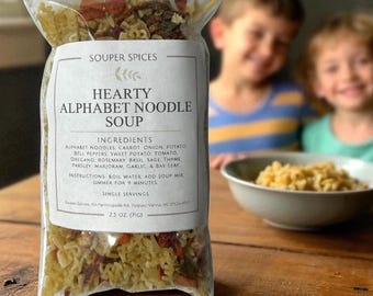 Peut inclure: Un sachet en plastique transparent de mélange pour soupe Souper Spices Hearty Alphabet Noodle Soup contenant des nouilles alphabet séchées, carottes, oignons, pommes de terre, poivrons, patates douces et herbes. L'étiquette indique 71g.