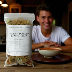 May include: A clear plastic bag of Souper Spices Tuscan Tomato Bowtie Soup mix. The label lists ingredients like bowtie noodles, broccoli, and tomato. A bowl of soup and a person smiling are in the background.