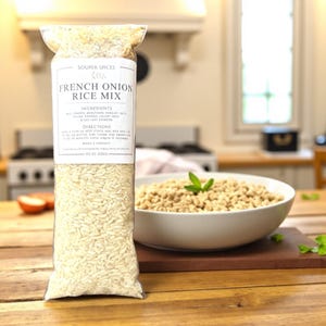 May include: A clear plastic bag filled with uncooked rice, labeled "French Onion Rice Mix." The ingredients and directions are listed on the label. A bowl of cooked rice and a sprig of basil are next to the bag. The bag contains 8 oz (226g) of rice.