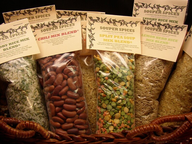May include: Six clear plastic bags filled with different dry soup and rice mixes. The bags are labeled with the name "Souper Spices" and the type of mix inside. The mixes include "Dry Rice Mix Blend", "Chili Mix Blend", "Split Pea Soup Mix Blend", "Savory Rice Mix", "Lemon Herb Rice Mix Blend".