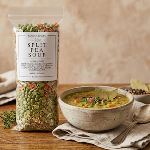 May include: A clear plastic pouch of Souper Spices Split Pea Soup mix containing green split peas, dried carrots, and herbs, labeled 6.0 oz (170g). Next to it is a ceramic bowl filled with prepared split pea soup garnished with herbs and bacon.