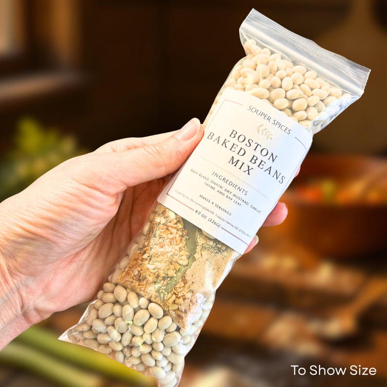 May include: A clear plastic bag filled with white beans and a mix of spices, labeled "Boston Baked Beans Mix" by Souper Spices. The label lists ingredients like navy beans, onion, dry mustard, garlic, thyme, and bay leaf. The bag contains 8 oz (226g) of product.