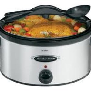 May include: A silver slow cooker with a black lid and a black handle. The slow cooker has a round shape and a black dial on the front. The slow cooker is filled with food, including a whole chicken, vegetables, and onions.