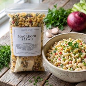 Könnte beinhalten: Ein durchsichtiger Plastikbeutel mit einer trockenen Makkaroni-Salat-Mischung und einem weißen Etikett mit der Aufschrift Souper Spices Macaroni Salad und 226g, neben einer Keramikschüssel mit zubereitetem Makkaroni-Salat mit Kräutern.
