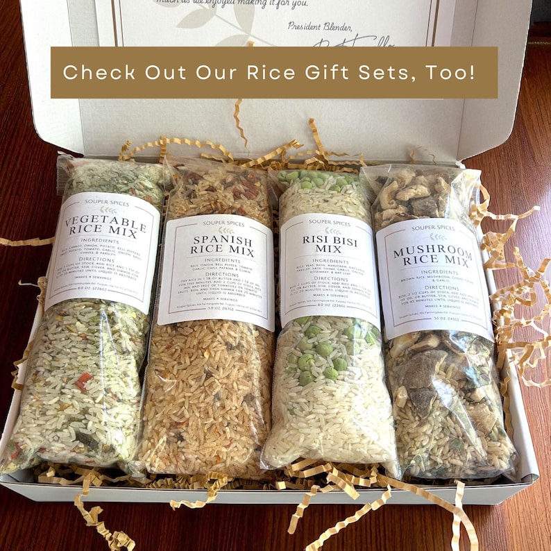 May include: A gift box containing four clear plastic bags of rice mixes: Vegetable, Spanish, Risi Bisi, and Mushroom. Each bag has a white label with the product name and ingredients. The box includes gold-colored paper filler and the text "Check Out Our Rice Gift Sets, Too!"