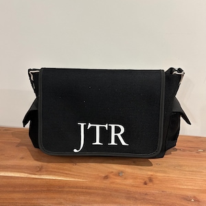 May include: Black canvas messenger bag with a white embroidered monogram "JTR".