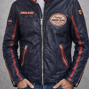 Könnte beinhalten: Marineblaue Lederjacke mit roten Akzenten und dem Schriftzug "ARMANI JEANS". Sie hat einen Reißverschluss, Reißverschlusstaschen und Aufnäher. Das Design der Jacke ist klassisch und sportlich.
