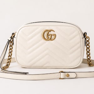 May include: Cream-colored, quilted leather crossbody bag with a gold-tone chain strap and a matching adjustable shoulder strap. The bag features a gold double-G logo on the front.