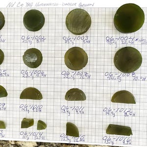 May include: An assortment of darker green, semi-translucent, and opaque Nd Ce YAG Hypo-inated samples. The samples are various shapes, including round, semi-circular, and rectangular. Each sample is labeled with a number and weight in grams.