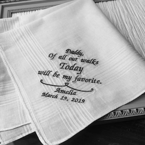 May include: White handkerchief with black embroidered text that reads "Daddy, Of all our walks Today will be my favorite. Amelia March 19, 2019".
